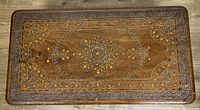 Top view of the rectangular wooden table showing detailed carved and painted floral pattern inlays in the center and border.