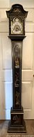 Full front view of black Chinese style tall grandfather clock with decorative painted panels and gold accents.