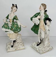 Pair of porcelain figurines - a woman and a man in green period clothing posed dancing.