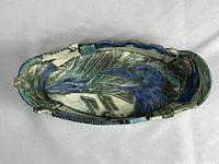 Top view of elongated ceramic dish showing carved bird design with blue and green painted details on cream base.