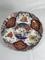 Front view of antique Imari porcelain plate showing traditional Japanese hand painted scenes and floral patterns with scalloped edges.