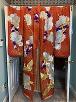 Full front view of reddish-orange kimono decorated with silver fans, gold cranes, and purple floral motifs