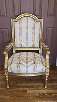 Full front view showing the giltwood carved frame with ornate armrests and arched back upholstered in striped brocade fabric.