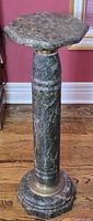Front view of the full green marble pedestal showing the octagonal top and round column with brass trim, sitting on wooden floor.