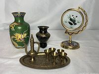 Full lot photo showing green cloisonné vase with yellow dragon, small dark brass vase with stand, panda decorative plate on crescent stand, brass teapot with tray and 5 cups.
