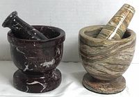 Two mortar and pestle sets, one red zebra jasper and one brown-toned marble, side by side on a white surface against a white background.