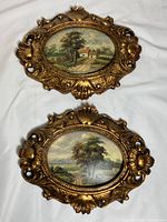 Two oval framed porcelain landscape plaques displayed on white cloth