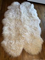 Full view of the cream colored irregular shaped sheepskin rug on wood floor, showing fluffy texture and natural fur pattern.