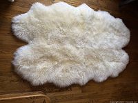 Top view of natural white sheepskin rug showing fluffy texture and irregular organic shape on hardwood floor.