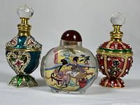 Photo showing all three snuff bottles: one glass with painted scene and two enameled metal bottles with jeweled decorations