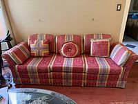 Front view of three-seater upholstered sofa with patterned red and gold fabric and three cushions.