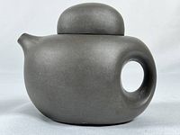 Full side view of the vintage Yixing Zisha clay mini teapot showing its rounded body and spout with circular handle and lid on top.