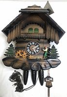Front view of vintage West German cuckoo clock showing chalet style with clock face, water wheel, pine cones weights and figurine