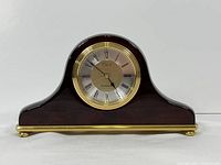 Front view of the full mantel clock showing dark wooden curved case with polished brass trim and feet.