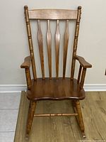 Front view of wooden rocking chair showing spindle back, armrests, seat, and rockers.