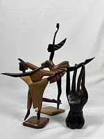 Group photo of three wooden sculptures, two abstract ballerinas and one hand sculpture, showing form and finish.