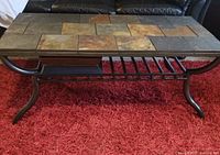 Rectangular coffee table with metal frame and removable multicolored stone tile top, shown on red carpet.