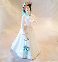 Front view of Royal Doulton Julia figurine in white dress with pink and black hat holding umbrella.
