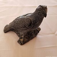 Photo of a dark faux soapstone bird carving with detailed feathers perched on a textured base, showcasing the overall item.