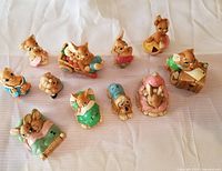 Group of 11 Pendelfin Bunny figurines arranged on white fabric, showing various poses and colors.