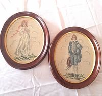 Pair of oval framed needlepoints on white fabric background showing Pinky and Blue Boy figures.