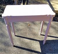 Front view of small pink painted flip-top table outdoors showing scalloped edges and straight legs.