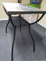 Side view of metal grey bar table frame with curved legs and lower slat shelf.
