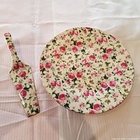 Cake plate and server side by side showing floral rose and green leaf pattern on white background.