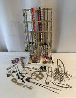 Full view of the mixed lot costume jewellery including chains hung on a display stand, and various necklaces, bracelets, and earrings laid flat on table.