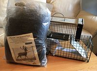 Photo showing two metal live animal traps on a wooden surface beside a sealed plastic bag of black nylon deer and animal fence.