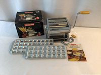 Full lot showing Mercator/Olympia pasta maker, two Raviolamp ravioli trays, instruction booklet, and original box