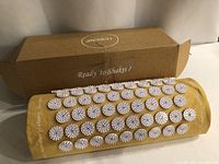 Shakti acupressure pillow lying in front of the cardboard box showing the acupressure discs and fabric.