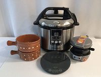 Photo showing all items in the lot including Paderno pressure cooker, breakfast sandwich maker, kitchen scale and terra cotta crocks