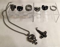 Photo showing eight stainless steel rings on display stand and two pendants on surface beside stand