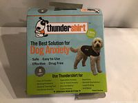 Front of Thundershirt box showing branding, slogan, dog model wearing shirt, and product features for dog anxiety relief