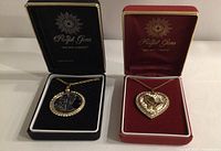 Two Royal Gems necklaces in original boxes, one round pendant with classical scene and one heart-shaped pendant with praying hands, both surrounded by man-made diamonds.