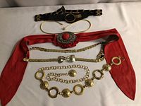 Full view of vintage belts displayed on white surface showing variety in materials and styles including red fabric and metal chain belts