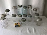 Overview of 14 vintage canning jars with lids and a box of rubber rings on white backdrop.