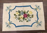 Full view of vintage handmade rug showing floral design with blue border on cream background.