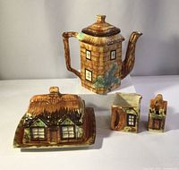 Full view of the set showing teapot, butter dish with lid, and two smaller house-shaped containers, all ceramic with cottage designs