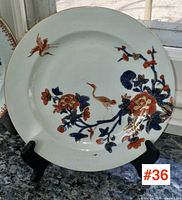 Front view of plate on stand showing overall design, including crane and floral motifs.