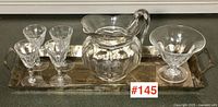 Set of four Waterford crystal sherry glasses, one crystal pitcher, silver serving tray, and small dish bowl displayed on dark surface.