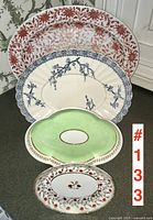 Four platters and trays arranged front to back: red transferware, blue and white porcelain, green scalloped, small white floral gilt tray