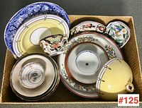 Overhead view of woven basket holding assorted porcelain plates, bowls and cups