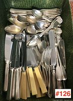 Wide view of assorted cutlery including knives, forks, spoons in a green basket