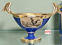 Frontal view of cobalt blue footed dish with gilt rim, wing handles and central rooster transfer titled la Vigilance.