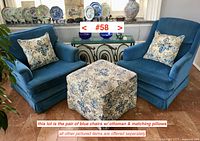 Pair of blue armchairs with ottoman and two pillows displayed in room.