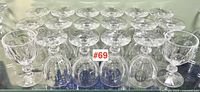 Eighteen clear crystal goblets arranged in rows on glass shelf