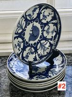 Stack of six blue and white Chinese export porcelain plates with central fish and botanical patterns, shown on granite surface with one plate on display stand.