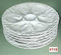 Stack of six white oyster plates showing scalloped wells and central reservoir